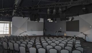 A spacious auditorium space featuring rows of chairs, large screens, and a stage area, designed for gatherings.