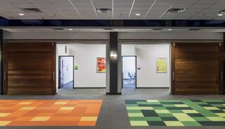 A hallway with two different colored carpet areas, orange and green, leading to multipurpose spaces with artwork.