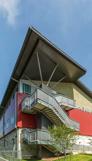 A children's ministry center with a sloped roof features a prominent staircase and a blend of red and gray exterior walls, surrounded by greenery.
