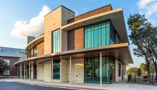 A modern, baptist church building featuring large glass windows, a mix of stone and brick, and a curved facade, set against a clear sky.