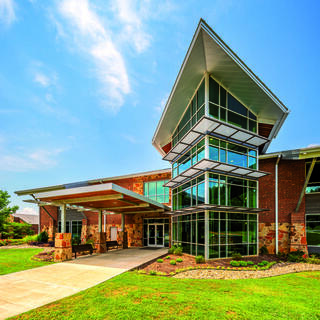A contemporary church facility features a unique angular roof, large glass windows, and a stone façade, surrounded by green landscaping.