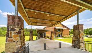A baptist church entrance features stone pillars and a spacious walkway under a wooden canopy, surrounded by lush greenery.