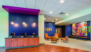 A lounge area features vibrant colors, stylish chairs, and lively artwork, creating an inviting atmosphere.