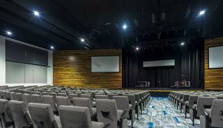A spacious worship center featuring rows of gray chairs, a wooden accent wall, and a stage with screens, ready for a performance or presentation.