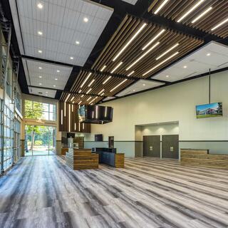 A spacious lobby features modern decor with wooden accents, large windows, and sleek flooring, creating a welcoming atmosphere.