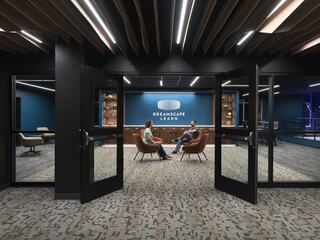 A modern learning space features two people seated in front of a vibrant blue wall with "DREAMSCAPE LEARN" signage, bathed in soft lighting.