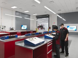 A bright workshop features two technicians at workstations, with modern equipment and screens, highlighting a focus on hands-on training.