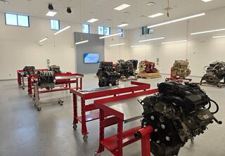 A well-lit training room at St. Louis Community College's new Transportation Education Center, designed by FGM Architects, features multiple engine assemblies on red workstations, with a digital display on the wall.