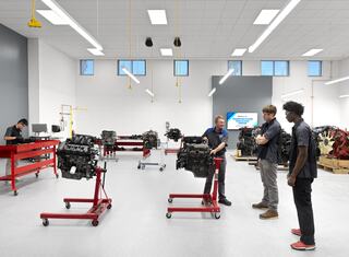 A workshop with several engine stands, where individuals are engaging in hands-on learning about automotive engines and repair techniques.