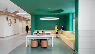 A vibrant space features a green accent wall, a stylish round light, and a combination of seating for relaxed study and interaction among kids.