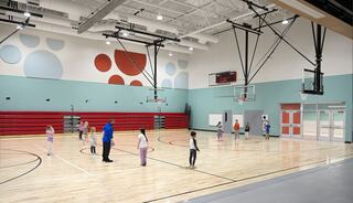A vibrant gymnasium features children engaged in activities under bright lighting, with basketball hoops and colorful wall designs.