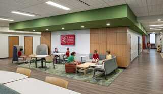 Interior of urban school at St. Austin Catholic School in Austin, Texas, with children sitting around a gathering area adjacent to a hallway, featuring flexible and varied furniture and finishings that offer movement and comfort.
