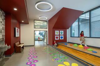 Interior look at St. Austin Catholic School hallway with raised nook/stage area adjacent to hallway and transition area. Graphics with alphabet letters and a colorful flower with numbers adorn the floor, inviting play and learning.
