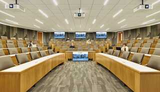 A modern lecture hall featuring wooden seating, multiple screens, and a spacious layout, designed for presentations and discussions.