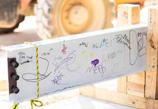 White steel beam sitting in wooden holder with colorful signatures