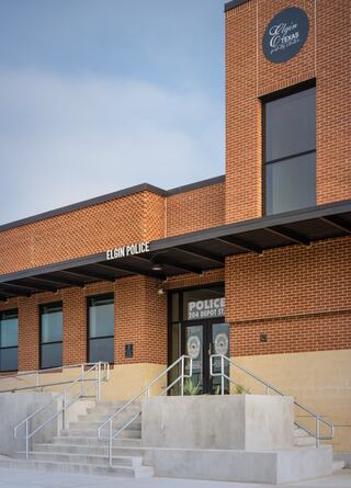 A modern brick building with large windows features signage for the Elgin Police Department, showcasing steps leading to the entrance.