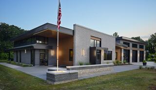 A modern building featuring a mix of brick and metal design, with large windows and an American flag prominently displayed in front.