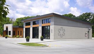 A modern, two-tone building with large glass windows, featuring an asterisk logo, surrounded by a landscaped area and a spacious parking lot.