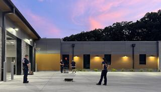 Four individuals engage in a casual game outside a modern building as the sky glows with sunset colors. Trees frame the background.