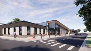 A modern single-story building features large windows, a sleek design, and a welcoming entrance, with pedestrians and vehicles nearby.