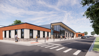 A modern, sleek building features a combination of brick and wood accents, with large glass windows and a landscaped street view.