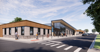 A modern building featuring a blend of stone and wood accents. The design includes large windows and an inviting entrance along a street.