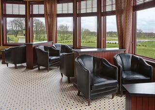 A cozy lounge area features elegant black chairs and large windows with a view of a peaceful landscape, creating a warm atmosphere.