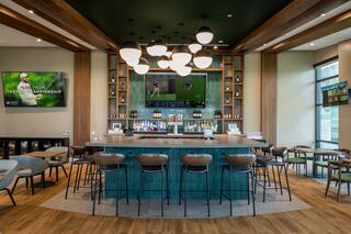 A stylish bar area featuring modern decor, a large TV, elegant lighting, and comfortable seating, perfect for socializing and watching sports.