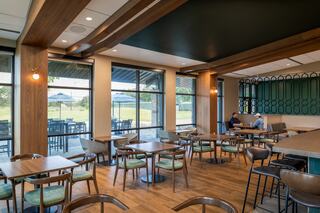 A modern café features wooden accents, cozy seating, and large windows showcasing an outdoor view with patio tables.