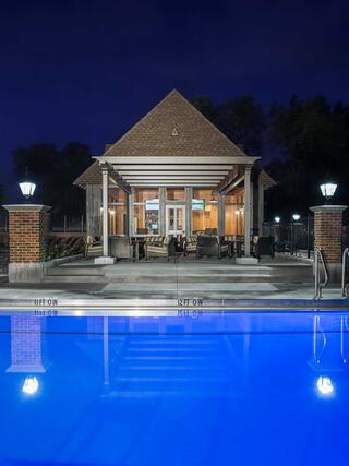 A serene pool scene at night, featuring a cozy pavilion with warm lighting and elegant reflections in the blue water.