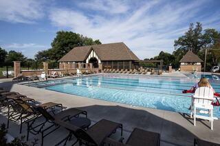 A serene pool area features lounge chairs, a spacious swimming pool, and a charming clubhouse, set against a clear blue sky.