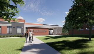 A modern college campus with a welcoming entrance, featuring a pathway leading to a building amid green lawns and clear blue skies.