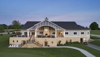 A modern clubhouse features a spacious patio and elegant architecture, set against a serene landscape at dusk.