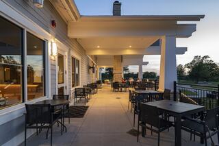 A spacious patio with black tables and chairs, illuminated in warm light, offers a relaxing setting for outdoor dining in a serene environment.