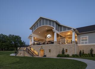A modern, elegantly designed building with a spacious entrance, illuminated at dusk, surrounded by lush greenery and steps leading up.
