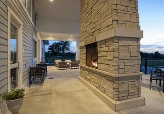 A cozy outdoor space features a stone fireplace, seating arrangements, and serene views, perfect for relaxation at dusk.