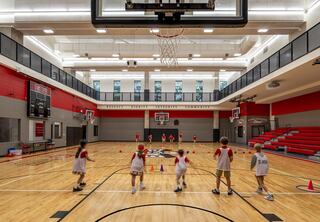 Children participate in a basketball practice session inside a spacious, well-lit gym, featuring multiple hoops and colorful cones.
