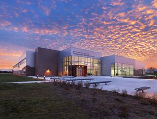Exterior look at the Southern Illinois University-Carbondale Transportation Education Center at dusk with pink highlighted clouds and tall glass walls of windows lit from the inside.