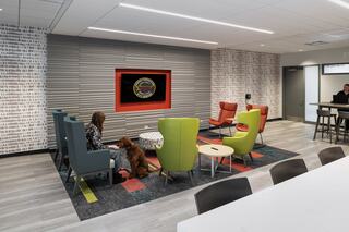 A cozy lounge area features colorful seating, a TV, and a person relaxing with a dog, creating an inviting atmosphere for socializing.