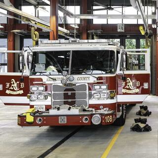 A fire station apparatus bay with a red fire truck and ambulance inside, showcasing modern architecture and natural lighting.