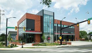 A modern fire station features a blend of brick and glass design, with landscaped surroundings, and a welcoming entrance.
