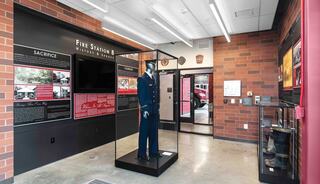 A display area featuring a firefighter's uniform in a glass case, with informational panels about the fire station's history and legacy.