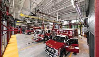 A modern fire station features multiple fire trucks and an ambulance, with efficient lighting.