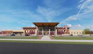A modern building design featuring a large entrance with a wooden canopy, surrounded by landscaped areas and parked cars.
