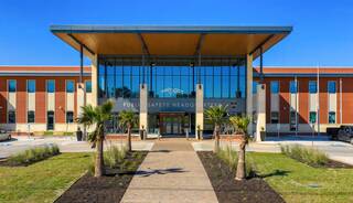 A modern public safety headquarters featuring a glass facade, lush landscaping, and a welcoming entrance with palm trees.