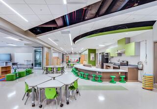 A modern classroom featuring flexible seating, a kitchenette, and vibrant green accents, fostering an engaging learning environment.