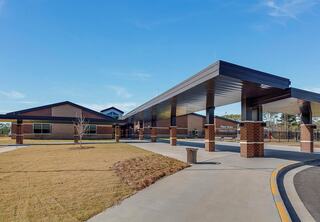 A modern building features a welcoming entrance, brick exterior, and a landscaped walkway, set against a clear blue sky.