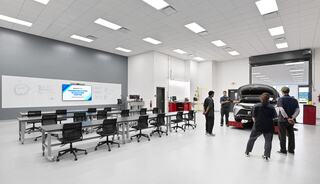 A modern automotive training facility features workstations, a vehicle under inspection, and individuals engaged in a learning environment.