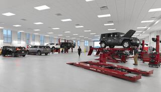 A spacious automotive workshop features several vehicles on lifts, with mechanics working and tools organized for efficient service.