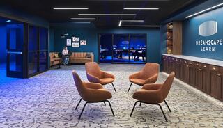 A modern, inviting lounge area features stylish chairs, a cozy couch, and a sleek wall displaying "DREAMSCAPE LEARN," with soft blue lighting.